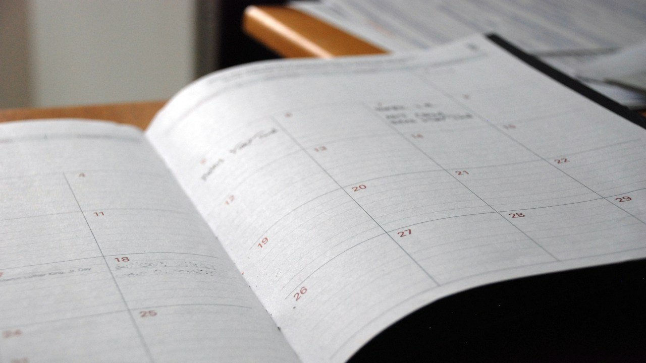 Contoh content calendar bulanan: planner kalender terbuka di atas meja kerja